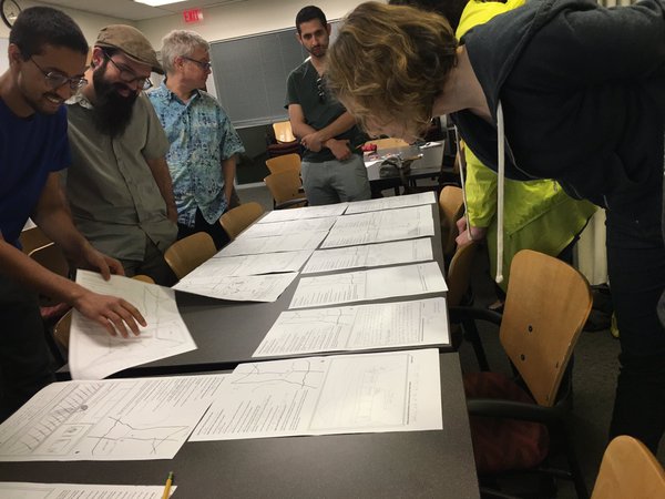 People look at maps and sketches laid out on a table.