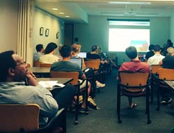 July meetup thumbnail. Open Austin members sitting in a dark library room facing the projected screen from July's meetup.